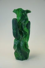 A sculptural green glass vase with a cactus and flowing wave motif, photographed against a neutral light gray background.