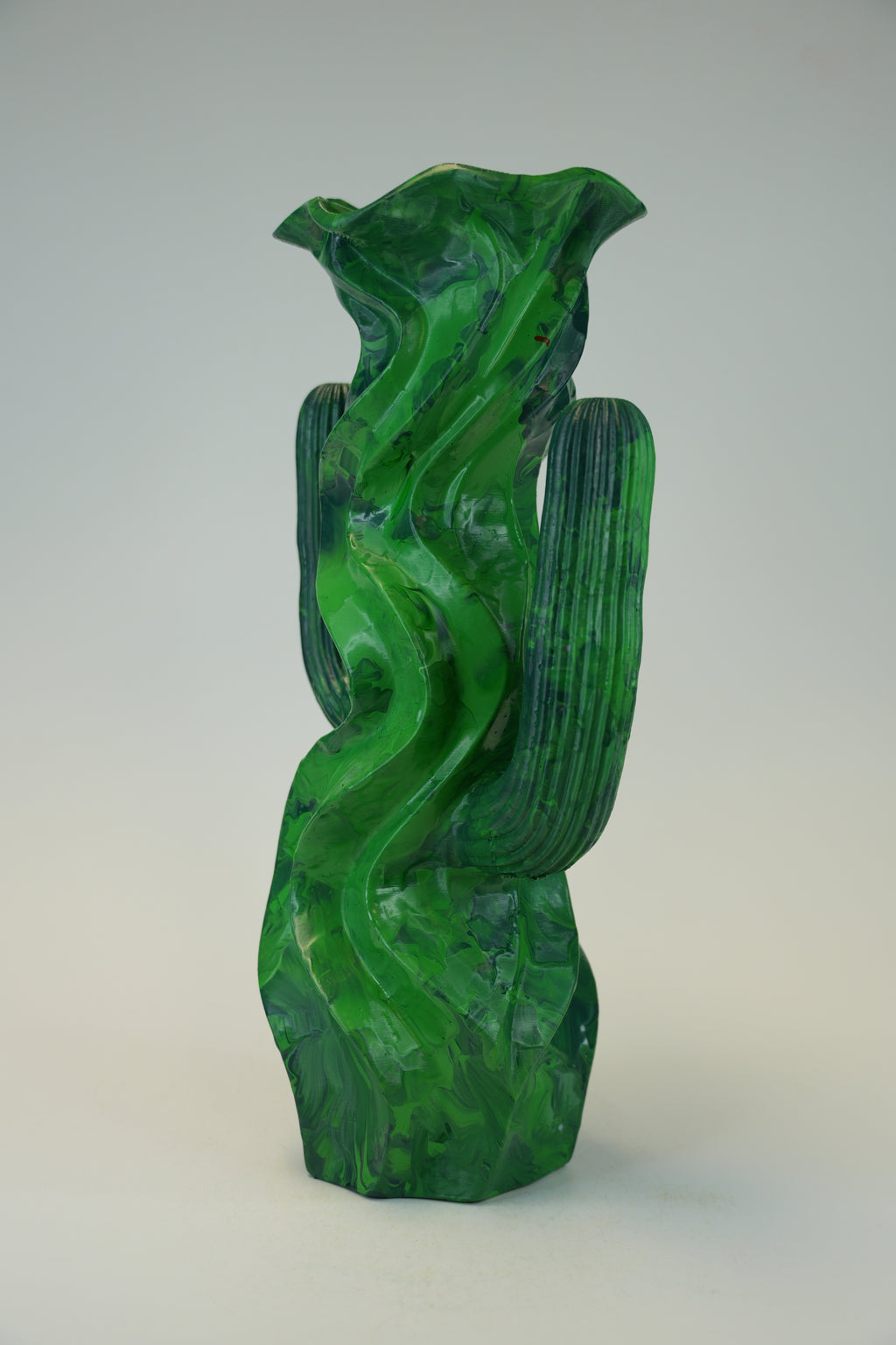 A sculptural green glass vase with organic, flowing wavy lines and ribbed vertical sections, photographed against a neutral light gray background.