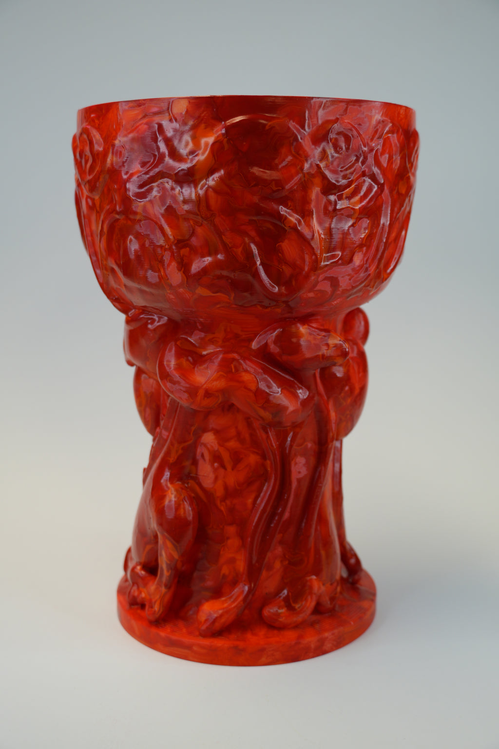 A glossy red carved decorative pedestal bowl or vase with an ornate sculpted base, photographed against a light gray studio background.