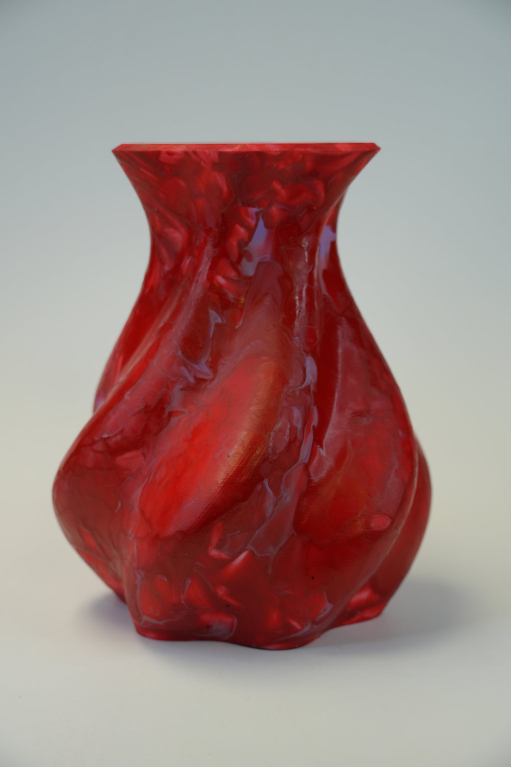 A glossy red sculptural wall-mounted vase with an organic, flowing form and a flared rectangular opening, shown against a plain light gray wall.