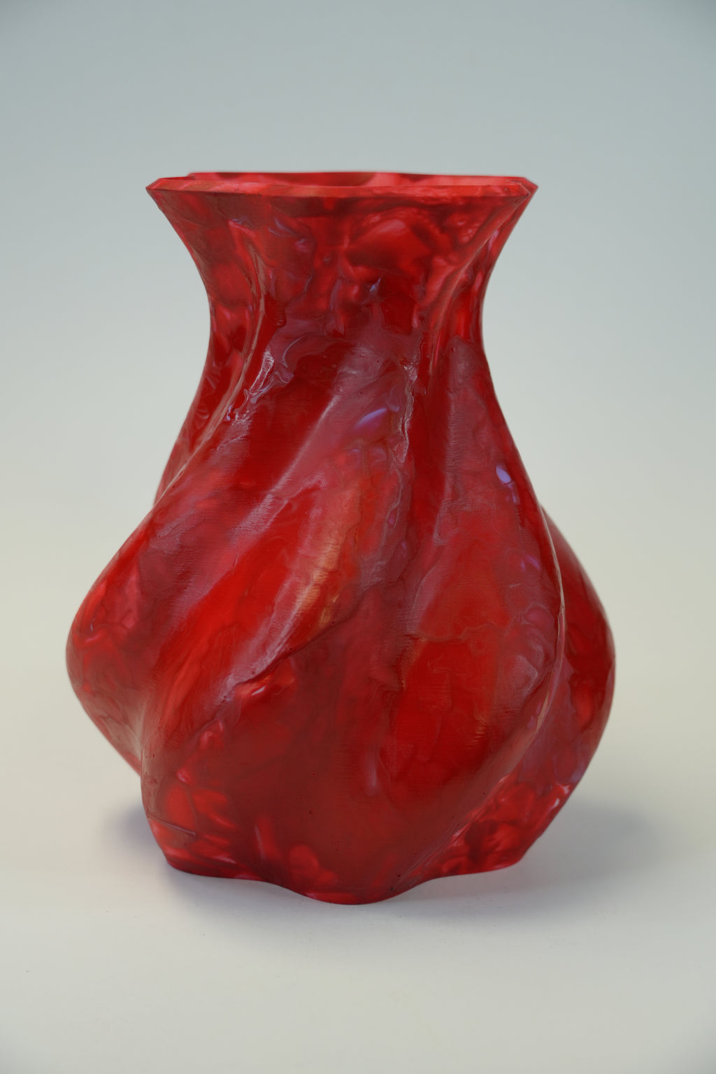 A glossy red sculptural vase with a wavy, organic form and flared rim, photographed against a plain light gray wall.