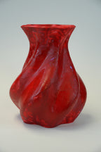A glossy red sculptural vase with a wavy, organic form and flared rim, photographed against a plain light gray wall.