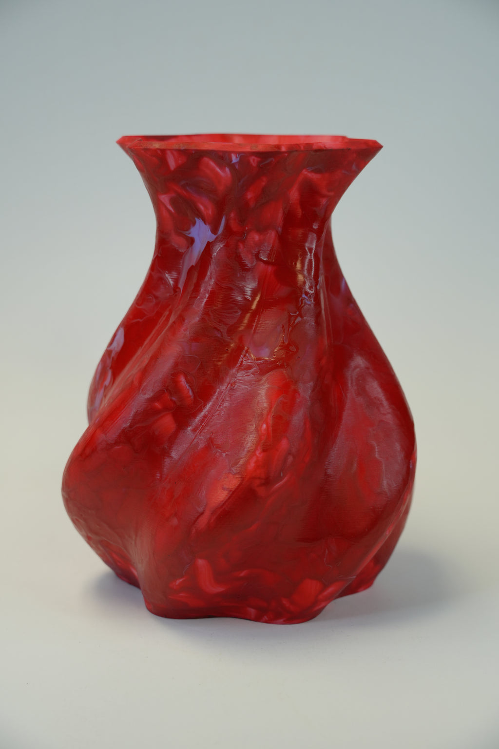 A glossy, textured red vase with a flared rim and organic, wavy contours, photographed on a neutral light gray background.