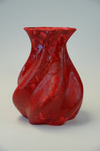 A glossy, textured red vase with a flared rim and organic, wavy contours, photographed on a neutral light gray background.