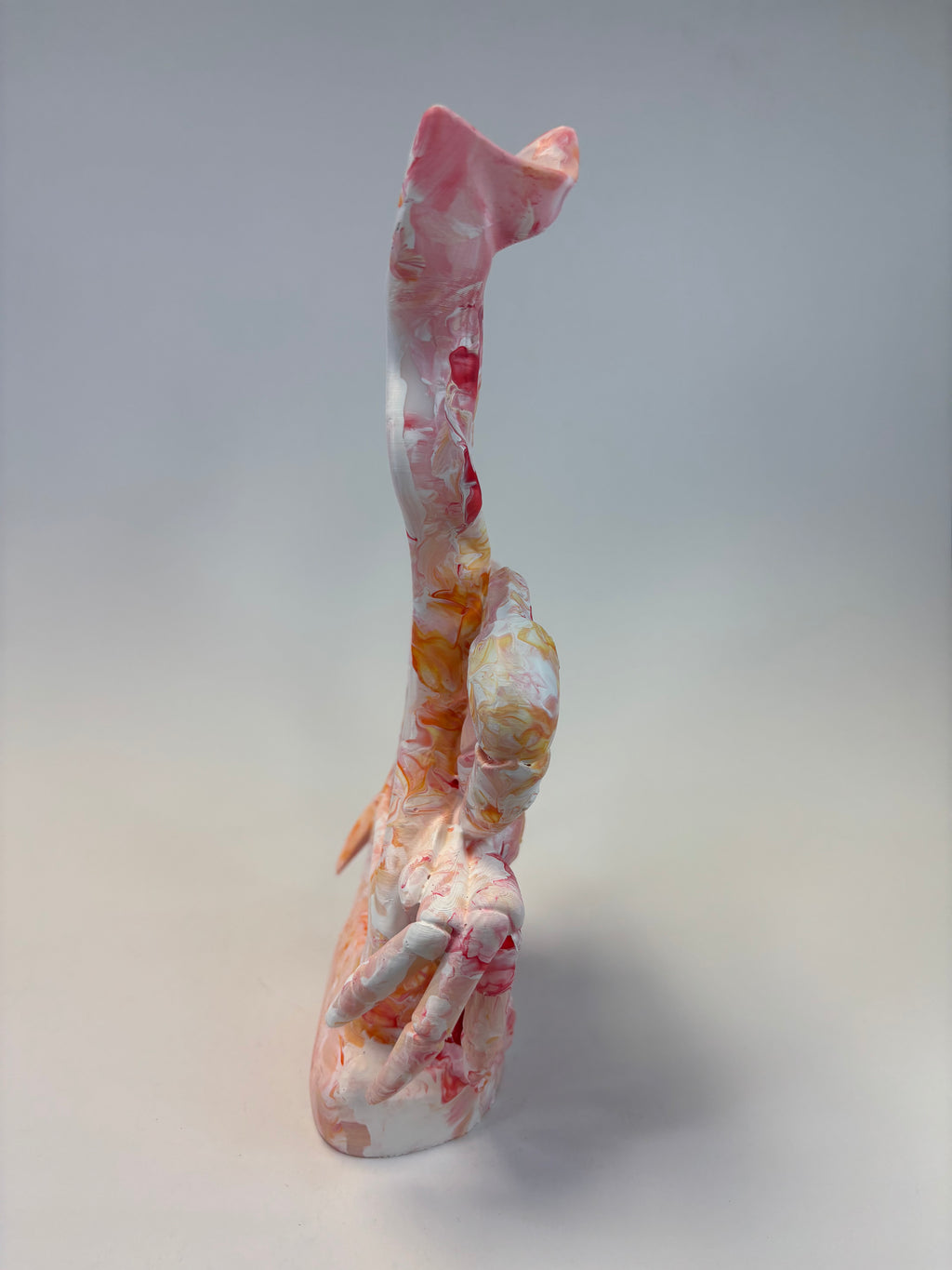 A tall, abstract sculptural decorative object with a curved, organic form, featuring a marbled pattern of pink, white, orange, and yellow on a light gray background.
