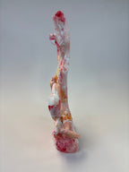 A tall, abstract sculptural decorative object with a marbled pattern of white, pink, red, and orange, photographed against a neutral light gray studio background.