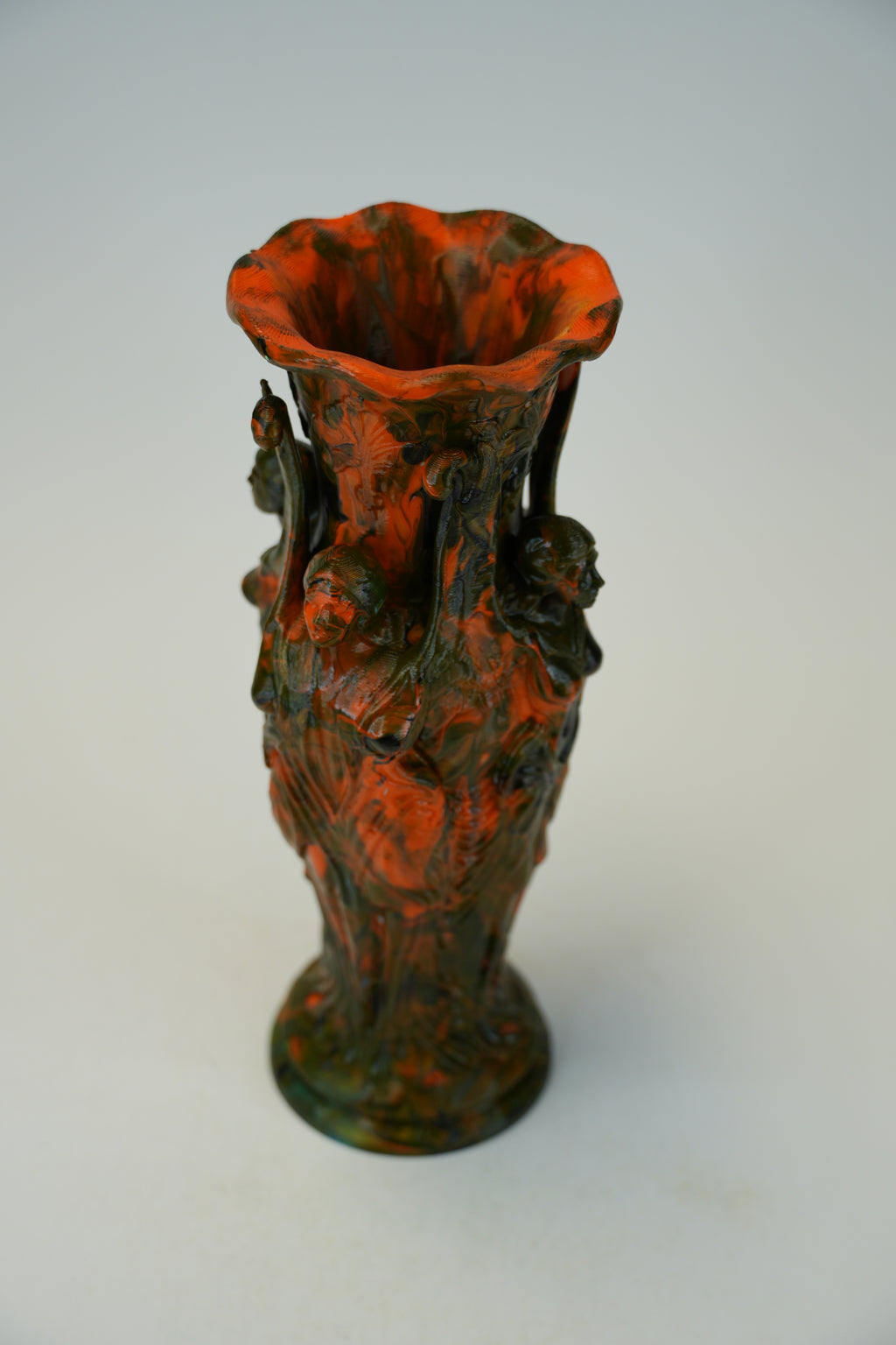 A decorative ceramic vase with a flared rim and sculpted side handles, featuring a mottled glaze of burnt orange-red and dark green on a light gray background.