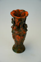 A decorative ceramic vase with a flared rim and sculpted side handles, featuring a mottled glaze of burnt orange-red and dark green on a light gray background.