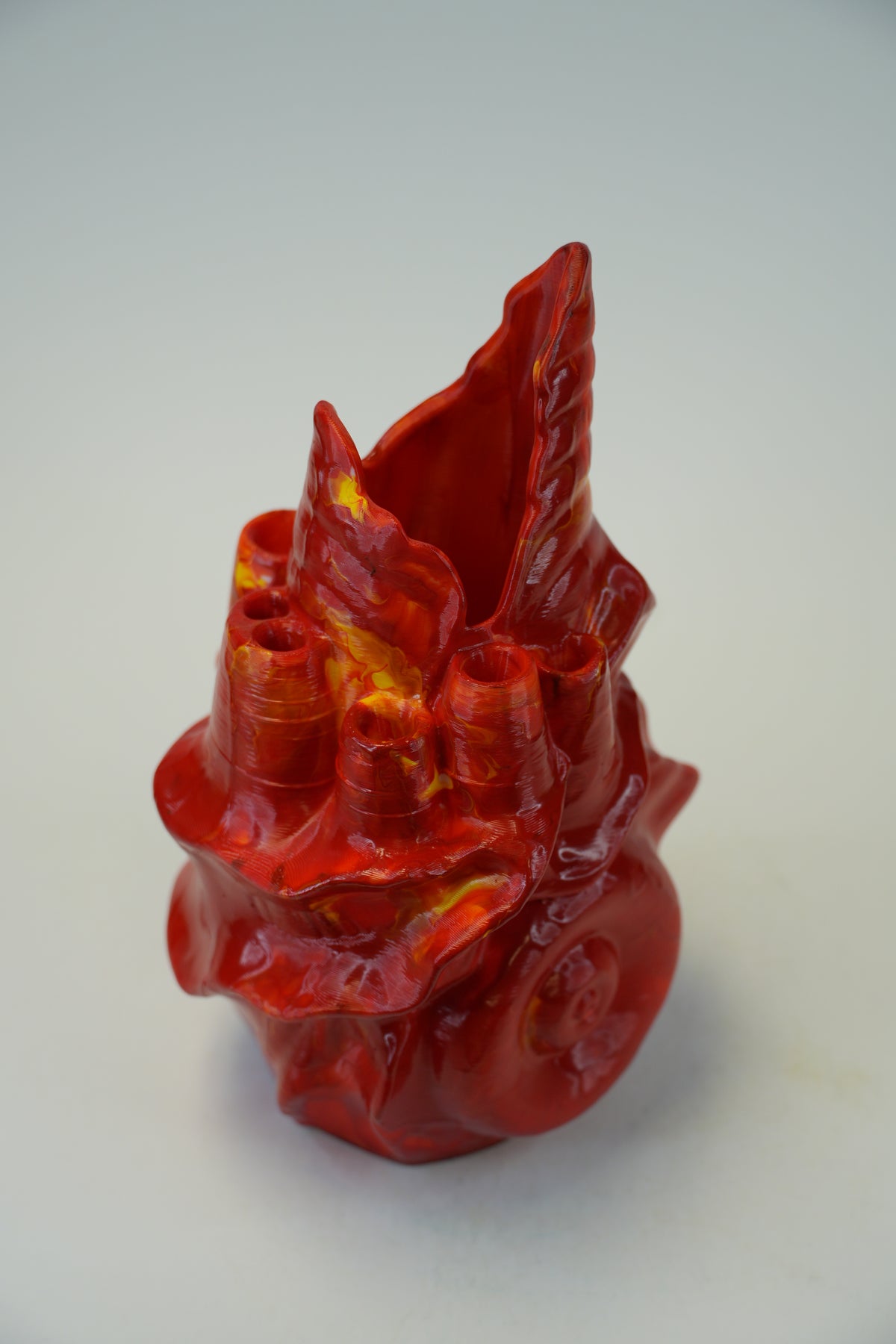 A glossy red sculptural ceramic vase with a textured, organic flame-like form and small yellow-orange highlights, photographed on a plain light background.