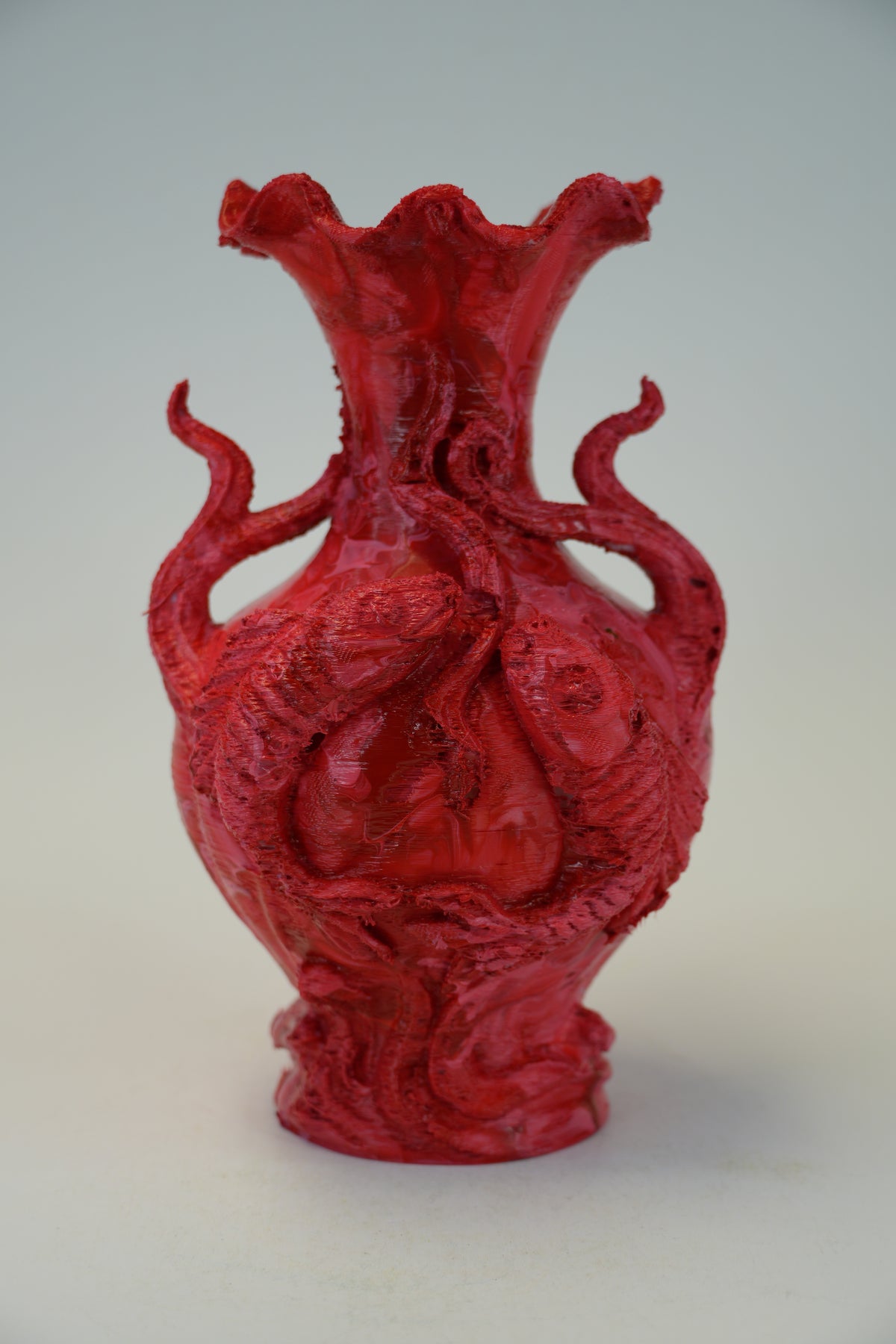 A vibrant red sculptural vase with organic, tentacle-like protrusions and a textured, organic surface, photographed against a neutral light gray background.
