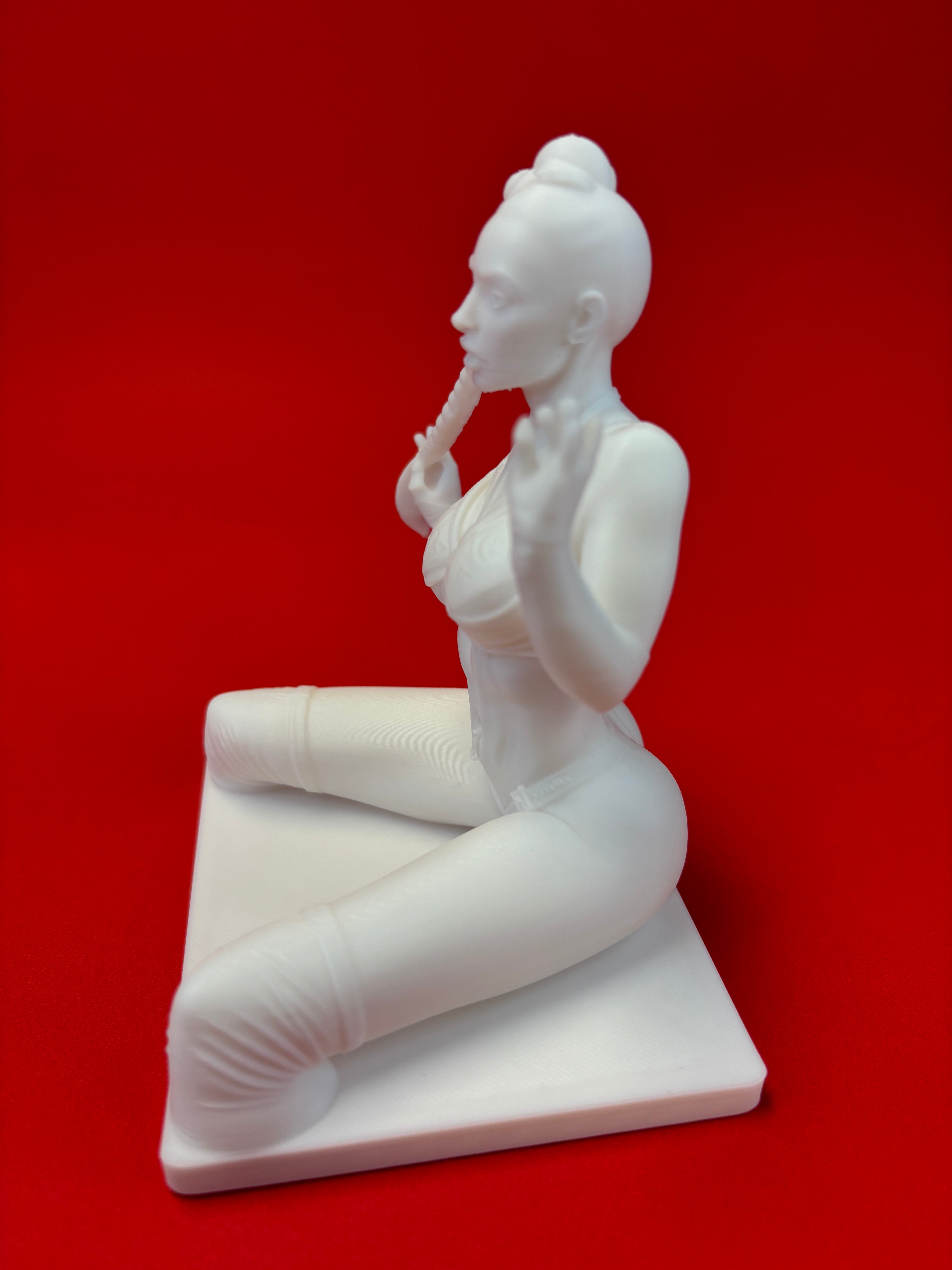 White sculpture of a seated figure on a red background