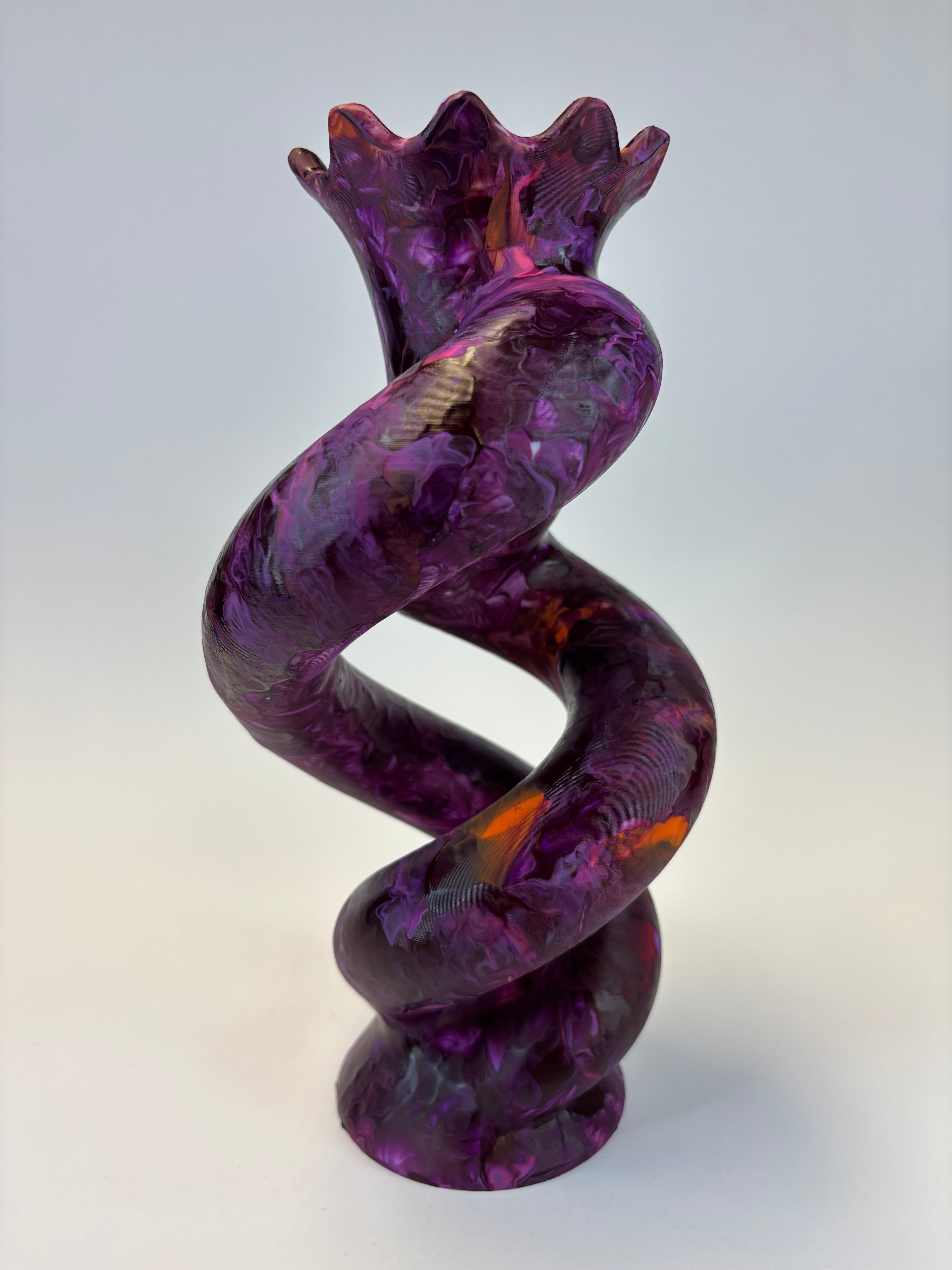 A sculptural spiral decor made of glossy, marbled purple glass with orange and lighter purple inclusions, set against a neutral light gray background.