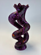 A glossy, twisted sculptural object in deep purple with marbled lighter purple and subtle orange highlights, photographed against a plain light gray background.