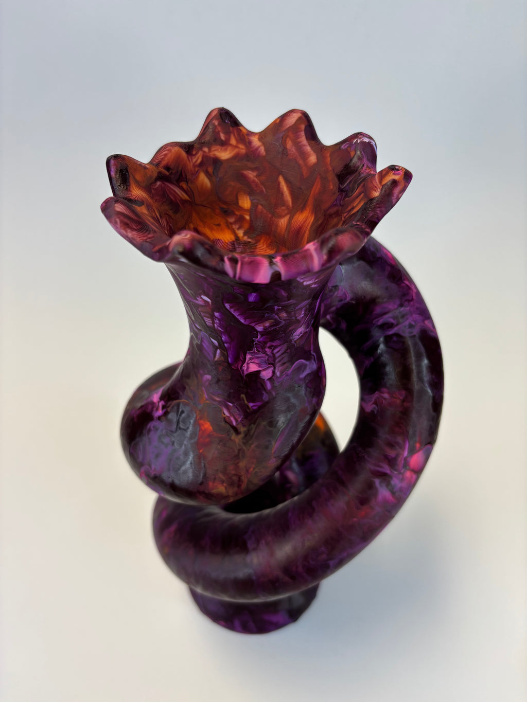 A sculptural spiral decor in marbled purple and amber-orange tones, photographed on a clean light gray studio background.