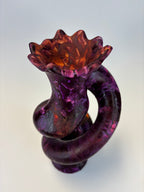 A sculptural spiral decor in marbled purple and amber-orange tones, photographed on a clean light gray studio background.