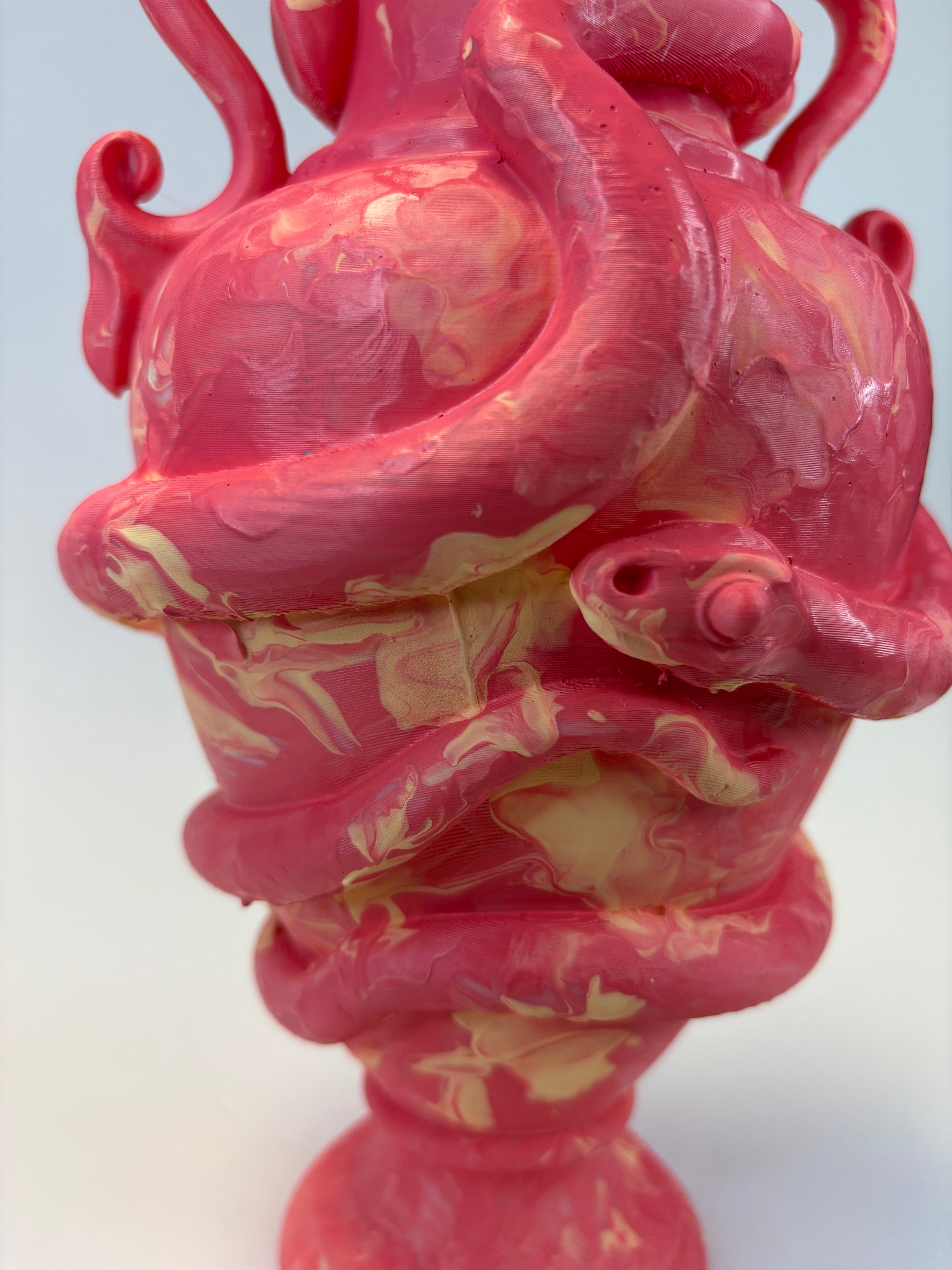 A close-up of a sculptural pink vase with a glossy finish, featuring organic marbled cream and pale yellow streaks throughout. The item has a bulbous top section with curling side details and a flared base, photographed against a plain light background.