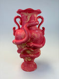 A pink and gold marbled ceramic vase with a flared rim, a bulbous body, and two curled handles, photographed on a plain light background.