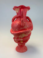 A red ceramic vase with a marbled pattern of cream and yellow, featuring a flared rim, two side handles, and a pedestal base, photographed against a neutral light gray background.