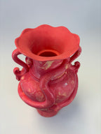 A pink ceramic vase with a wide flared rim, two curved side handles, and a sculpted snake wrapping around the body, shown on a light gray background.