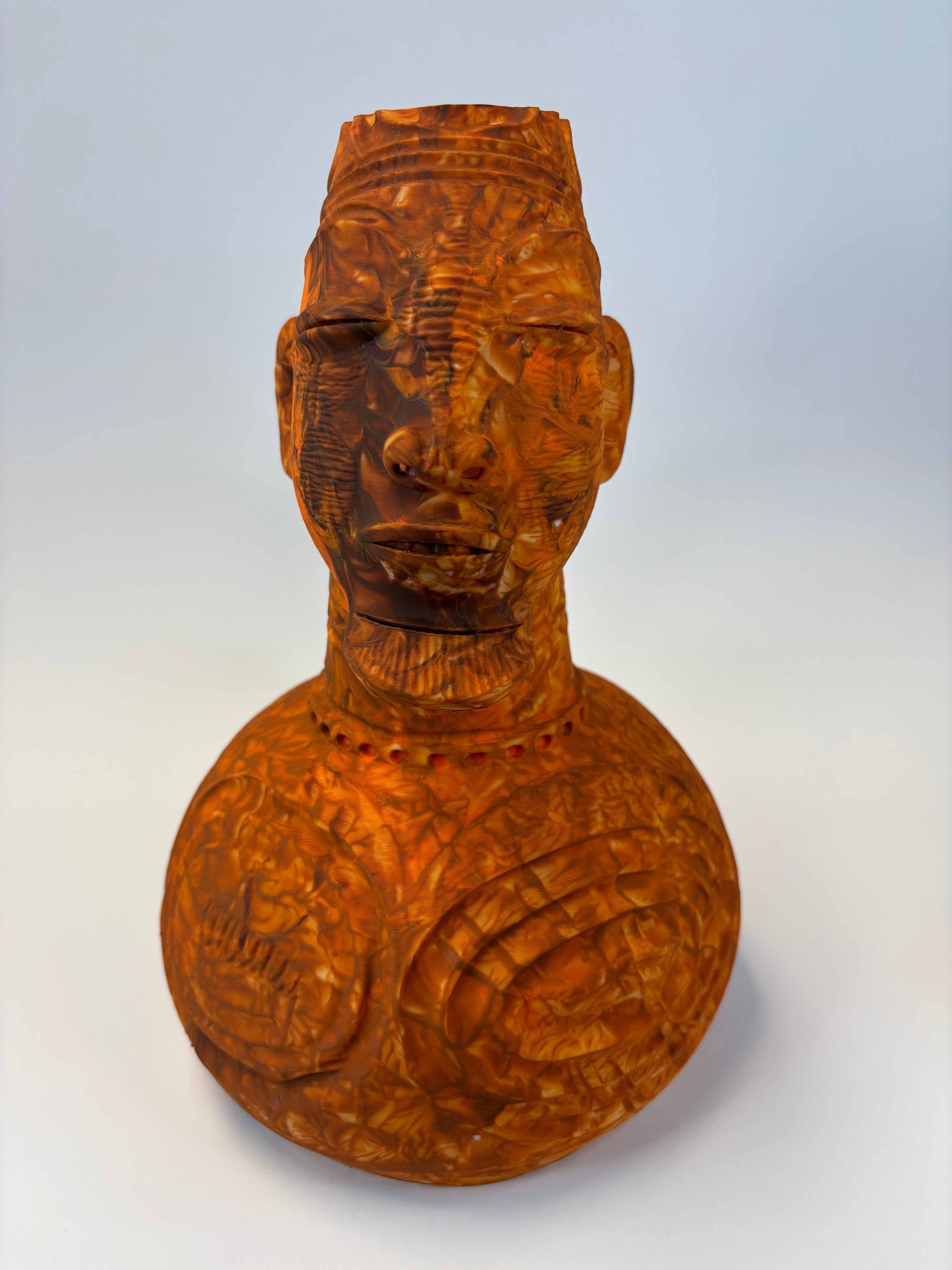 Wooden type clay like sculpture of a face with intricate carvings.