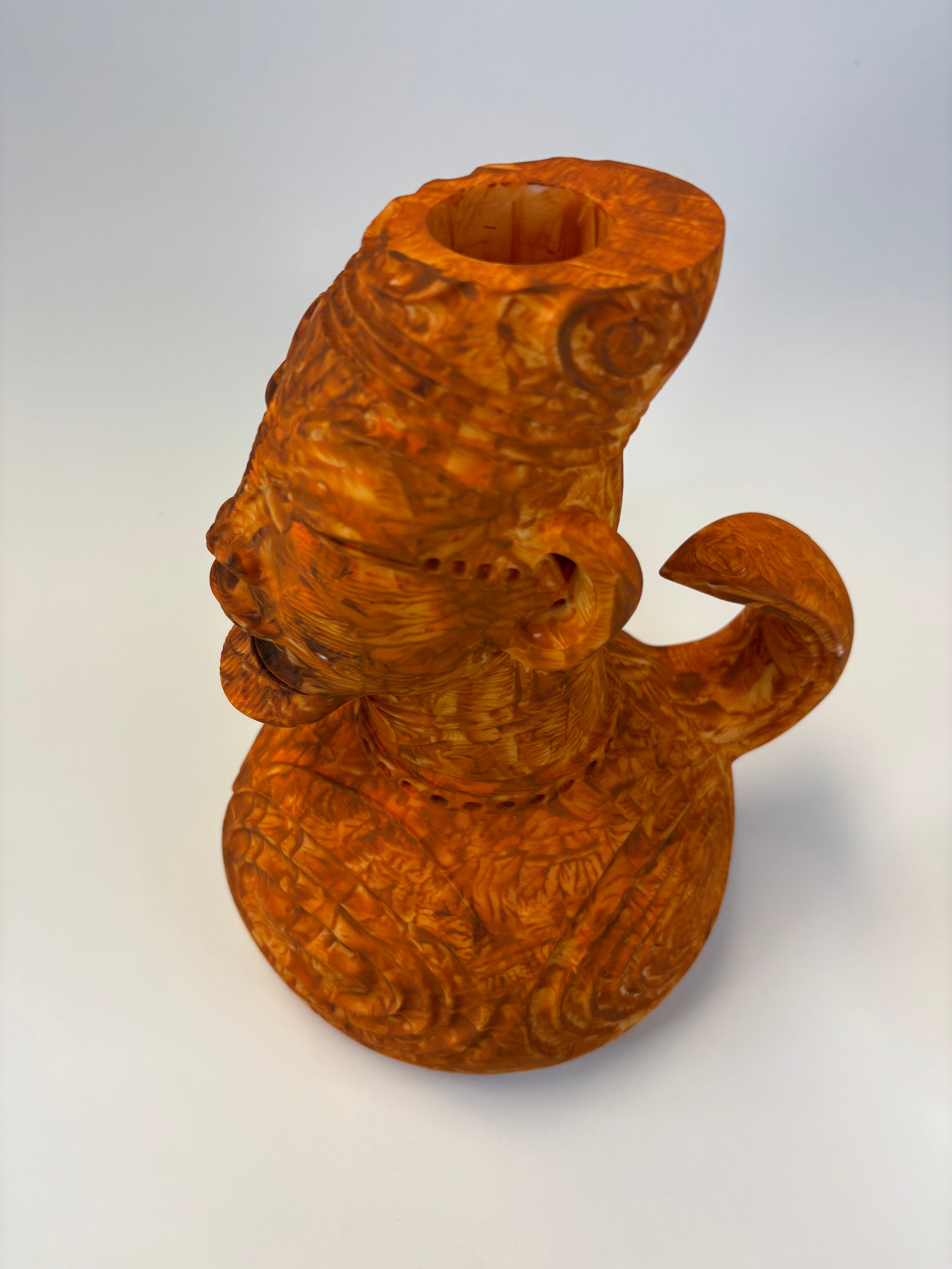 Wooden type clay like sculpture of a face with intricate carvings.