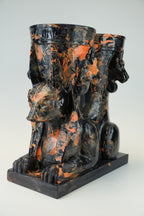 A sculptural black and orange marbled ceramic vessel set featuring a seated Anubis jackal motif on a rectangular base, photographed against a light gray studio background.