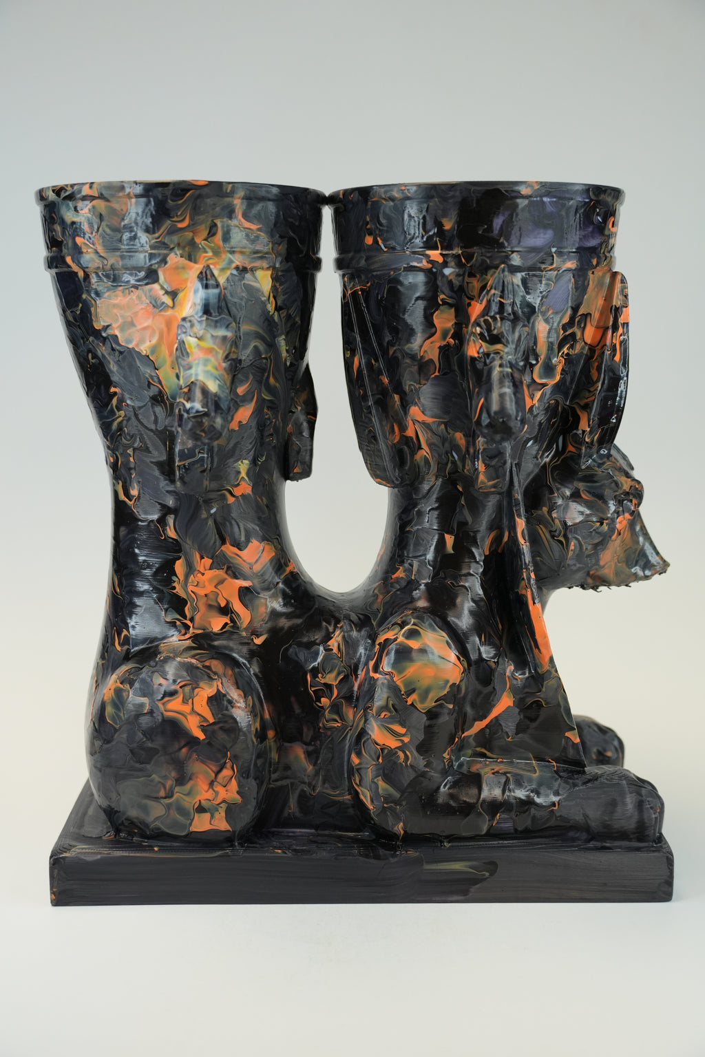 A sculptural black and orange marbled ceramic vessel set featuring a seated Anubis jackal motif on a rectangular base, photographed against a light gray studio background.