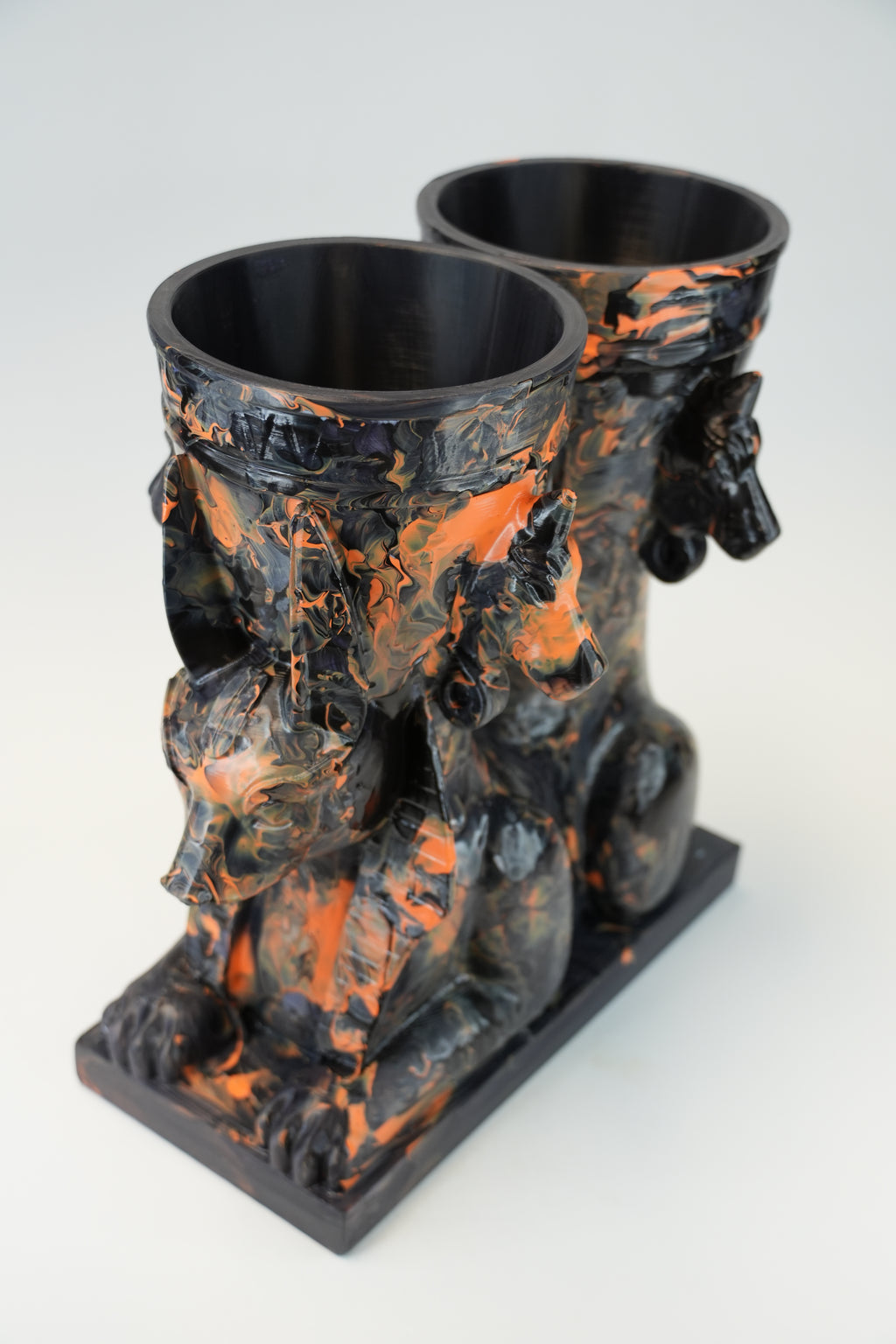 A sculptural black and orange marbled ceramic vessel set featuring a seated Anubis jackal motif on a rectangular base, photographed against a light gray studio background.