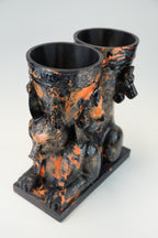 A sculptural black and orange marbled ceramic vessel set featuring a seated Anubis jackal motif on a rectangular base, photographed against a light gray studio background.