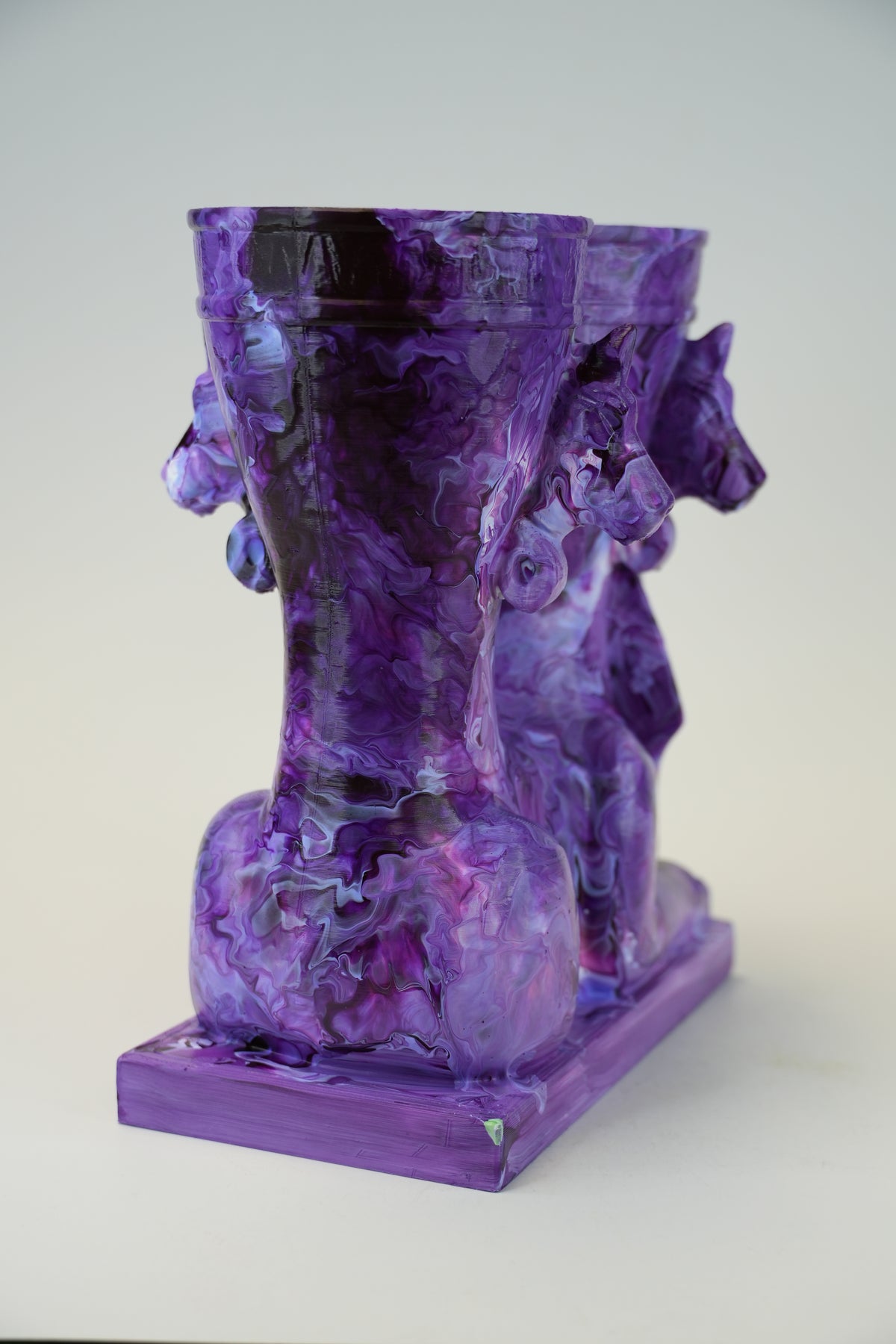 A purple resin sculpture of two stylized horses on a rectangular base, photographed against a plain light gray background.