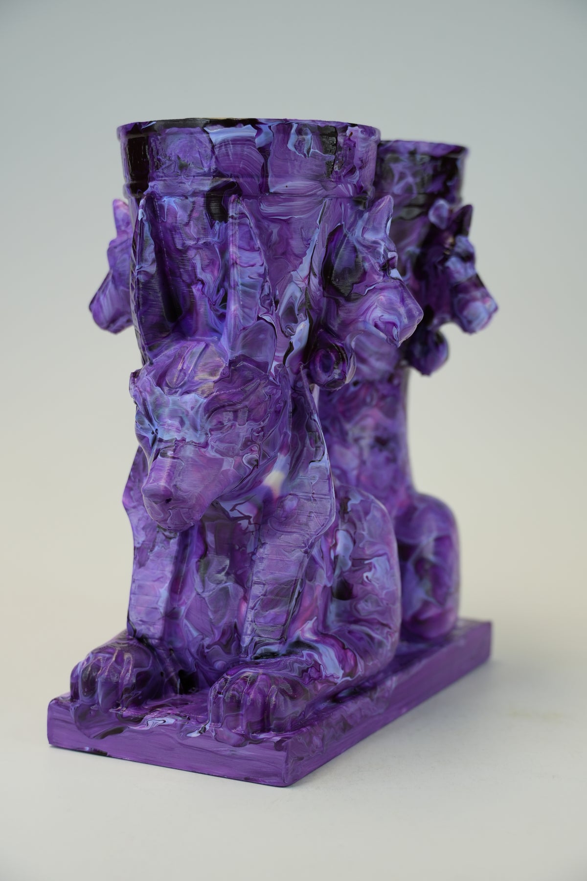 A purple sculptural candle holder featuring three stylized lion or gargoyle figures supporting three cup holders, set against a plain light gray background.
