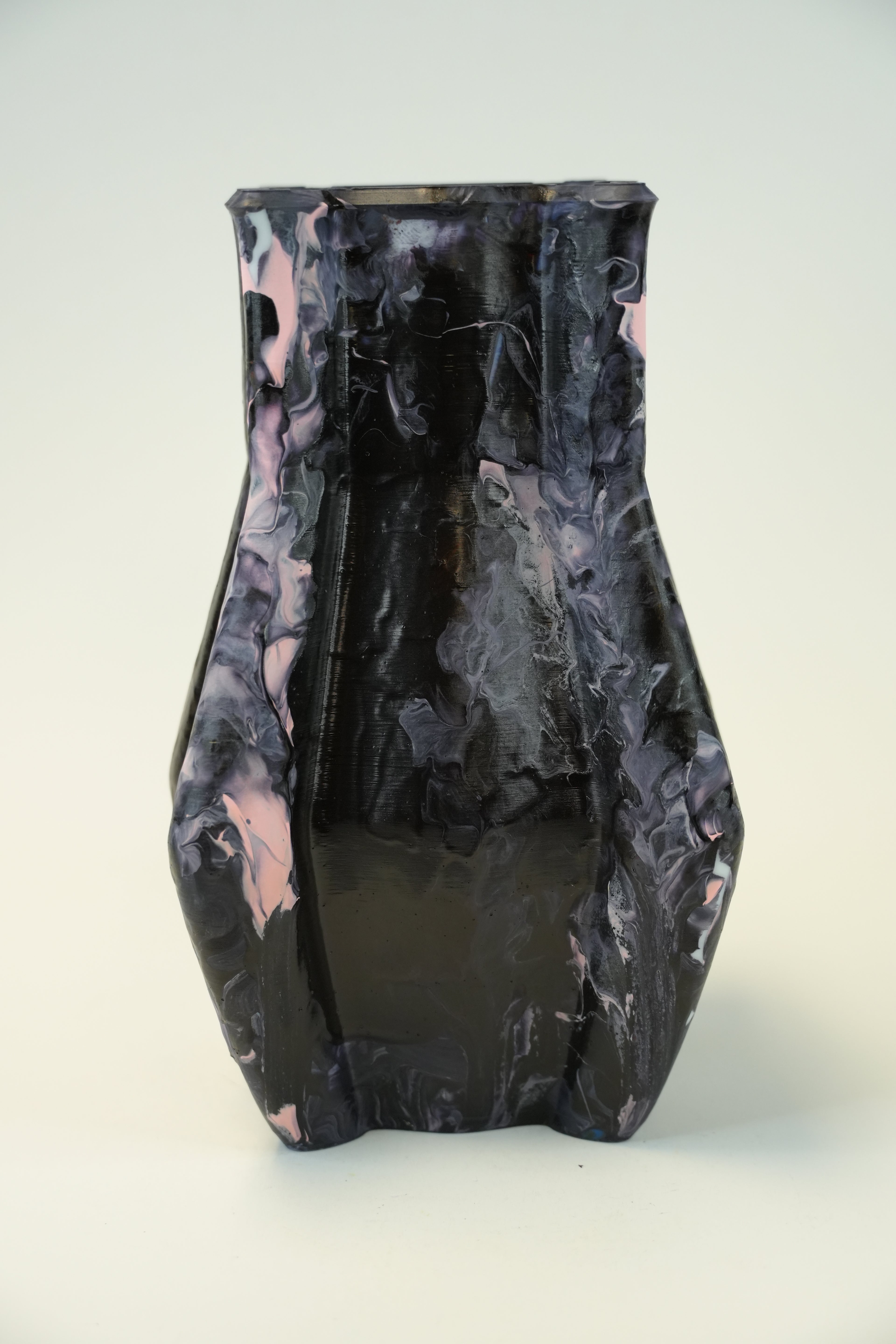 A sculptural ceramic vase with a glossy black base and marbled swirls of light pink and gray, photographed against a neutral off-white background.