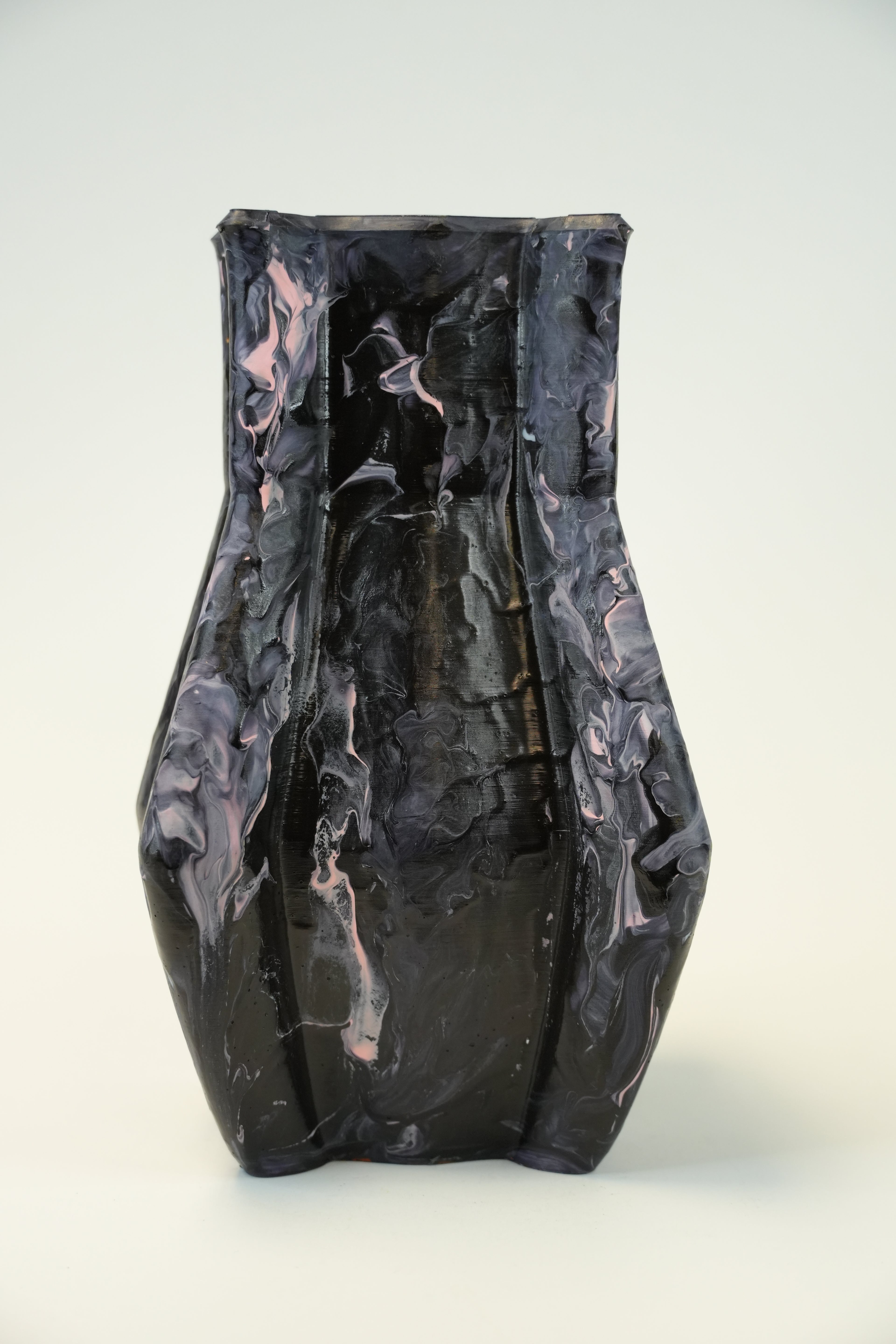 A sculptural black ceramic vase with a textured, marbled finish and subtle pinkish highlights, photographed against a neutral light gray background.