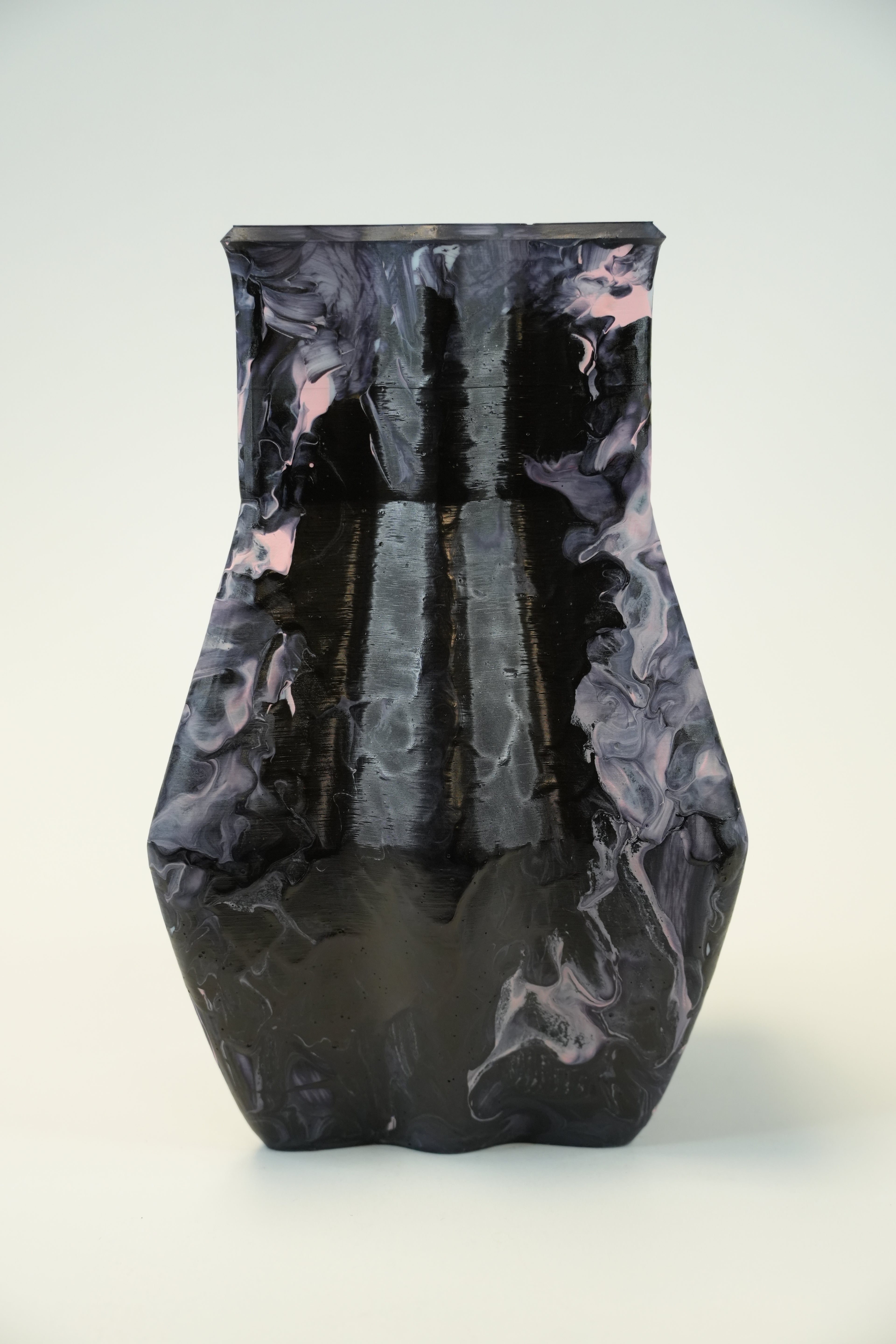 A sculptural ceramic vase with a glossy black and dark gray marbled pattern and subtle pinkish-gray veining, set against a plain light gray background.