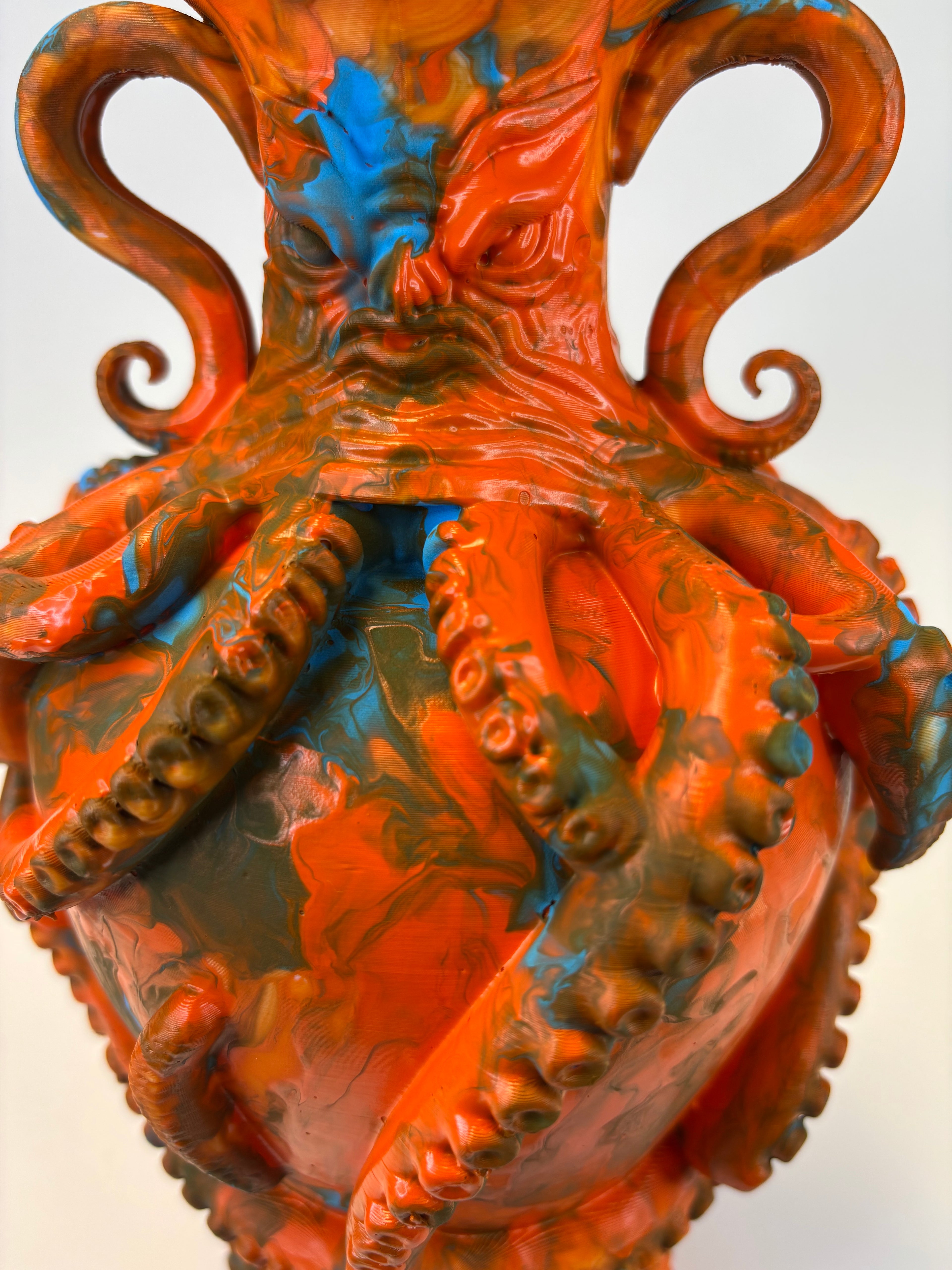 A close-up of a sculptural octopus vase with glossy orange, brown, and blue marbled paint details on a plain light background.