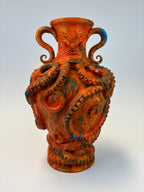 An orange and brown vase sculpted with an octopus design, featuring curled handles, suction cups, and blue accents, set against a light gray background.