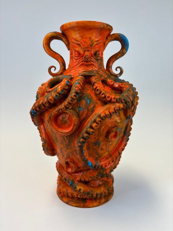 An orange and brown vase sculpted with an octopus design, featuring curled handles, suction cups, and blue accents, set against a light gray background.