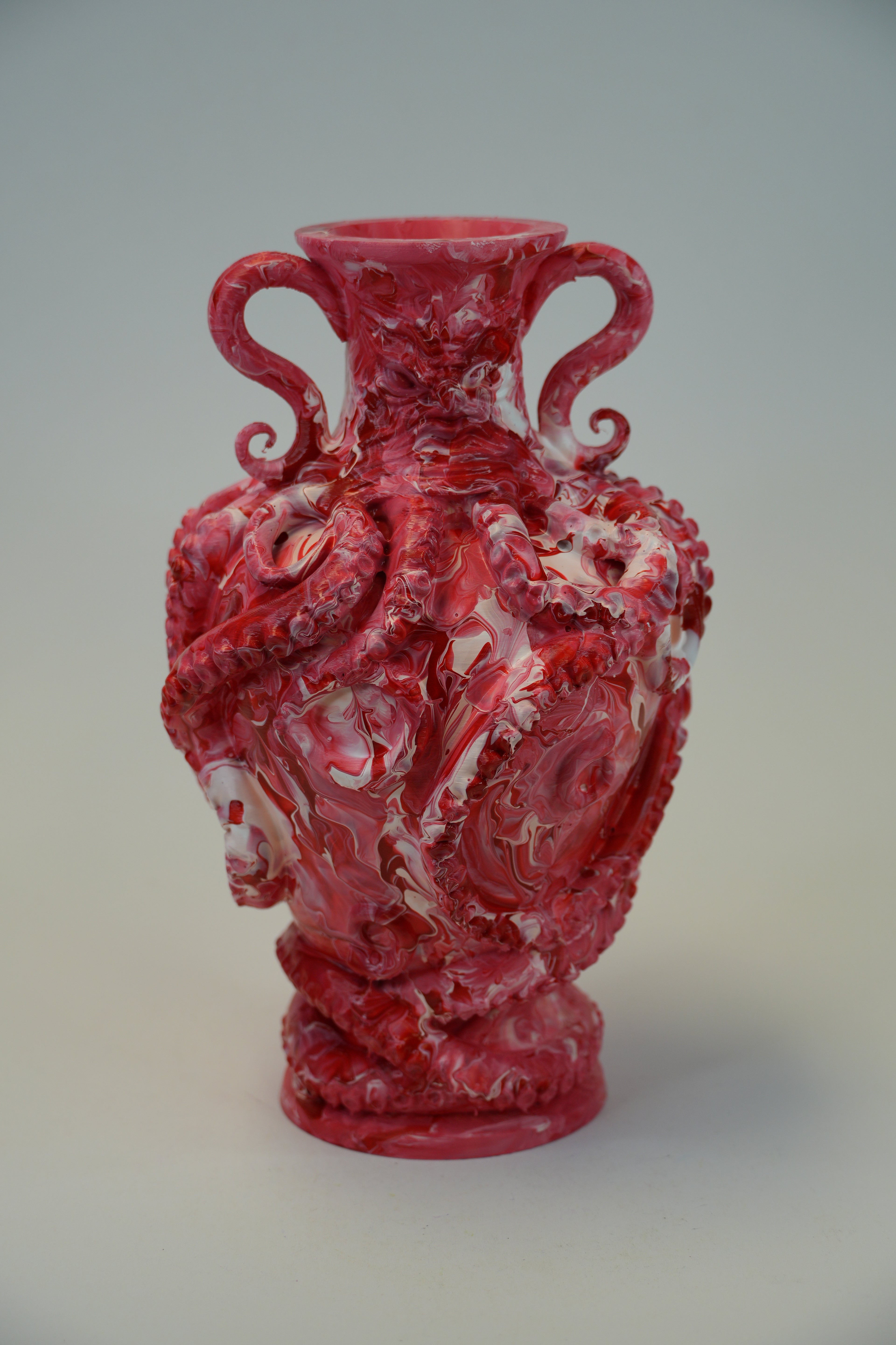 A red and white marbled ceramic vase with sculpted dragon motifs and two curved handles, photographed against a neutral light gray background.