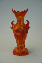 A sculptural glass vase with a flared rim and two side handles, crafted in a marbled orange, red, and yellow glass style, set against a neutral gray background.