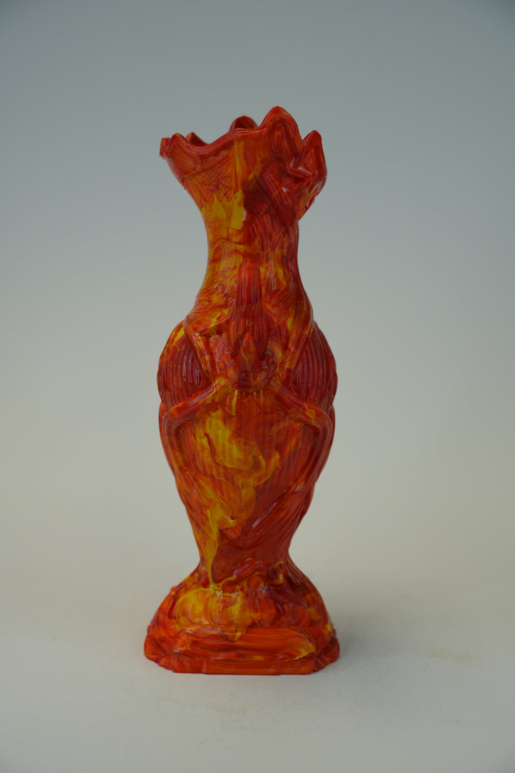 A sculptural ceramic vase with a textured, fiery design in red, orange, and yellow, standing on a neutral light gray background.
