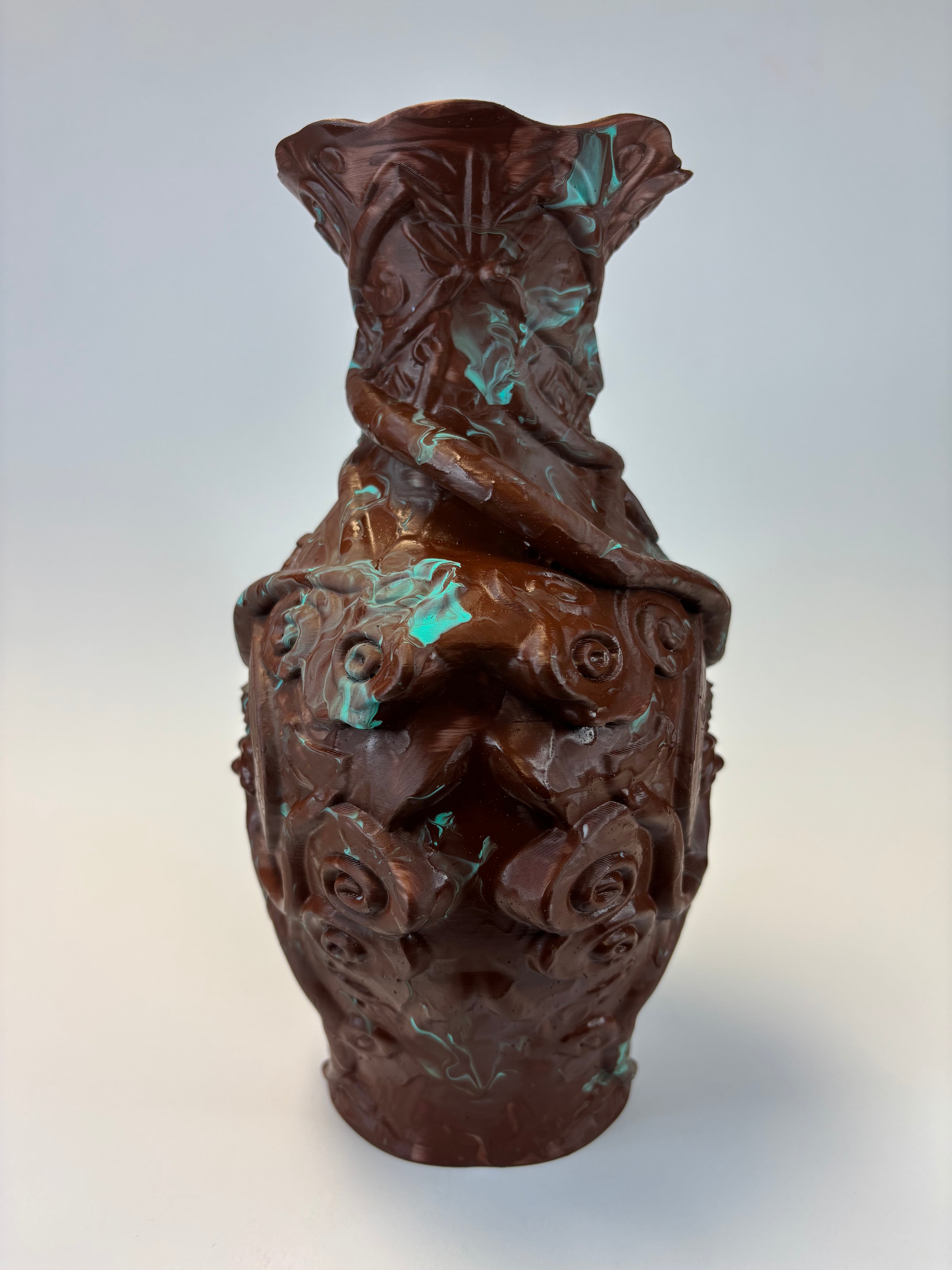A dark brown carved decorative object with a textured, organic surface and subtle turquoise patina highlights, shown against a plain light gray background.