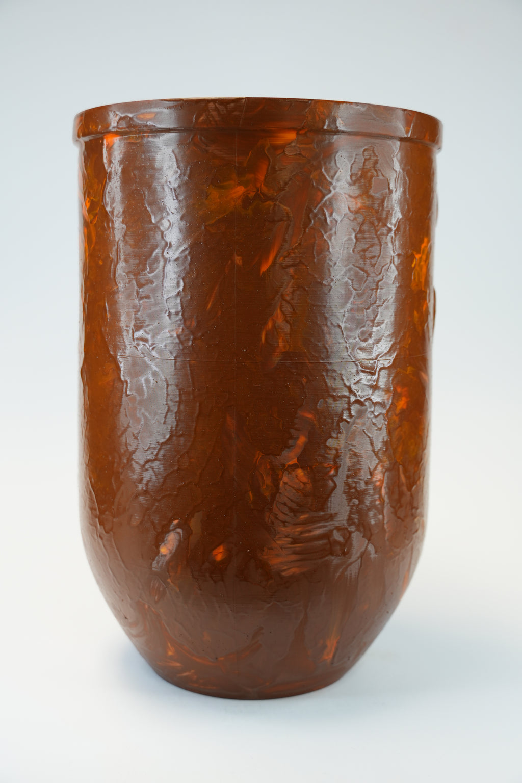 A glossy amber-brown textured vase with a rounded base, photographed against a clean light gray studio background.