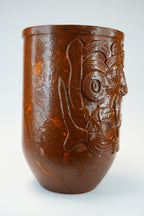 A brown translucent ceramic cup with a carved Aztec skull design on the side, photographed against a light gray background.