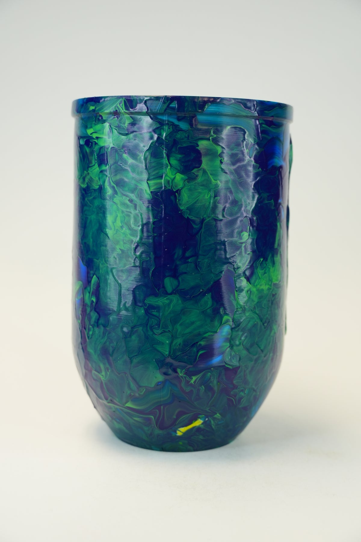 A glossy ceramic vase with an organic marbled pattern in deep blue, green, and purple, set against a plain light gray background.