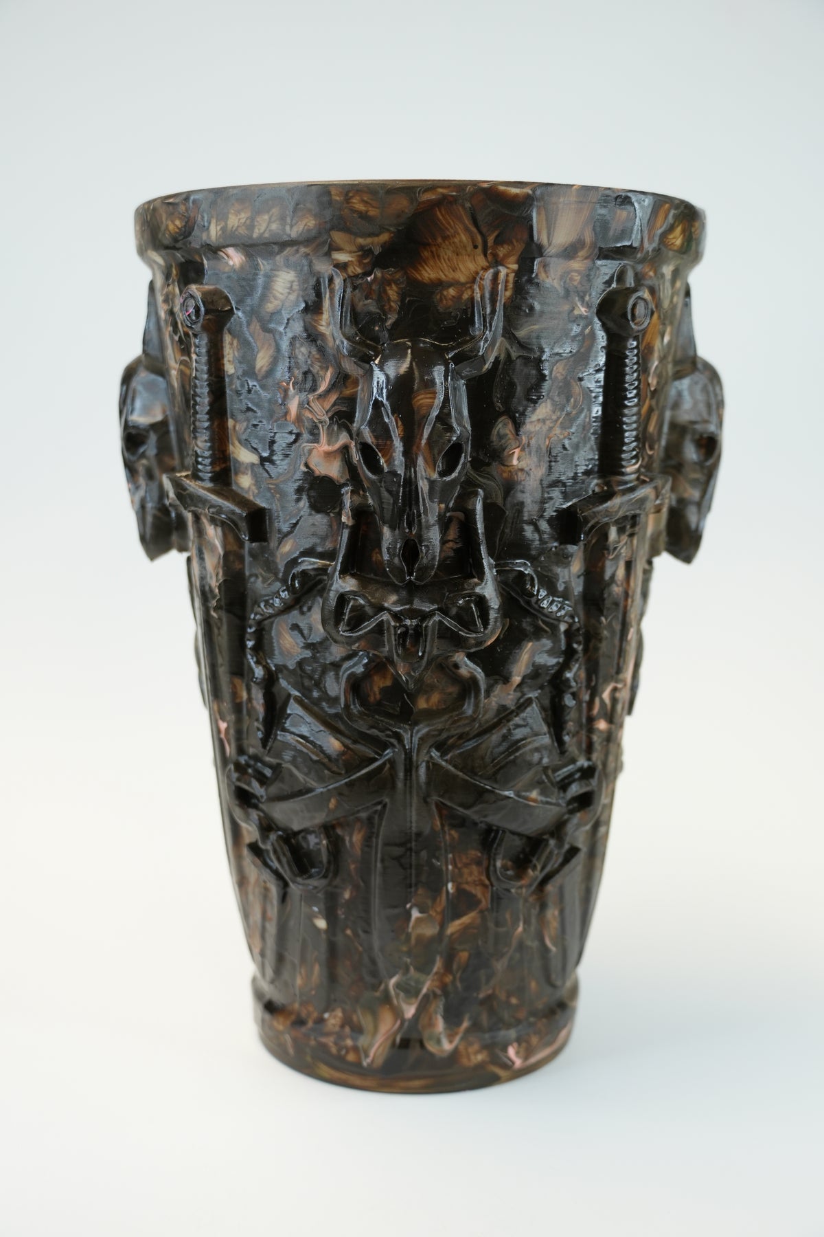 An ornate dark brown ceramic vase with a glossy finish, featuring sculpted relief details of winged cherubs and animal heads on the sides, set against a plain light gray background.