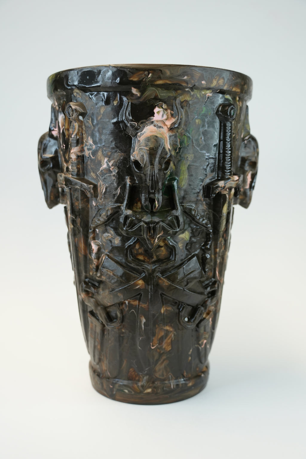 An ornate dark brown ceramic vase with a glossy finish, featuring sculpted relief details of winged cherubs and animal heads on the sides, set against a plain light gray background.