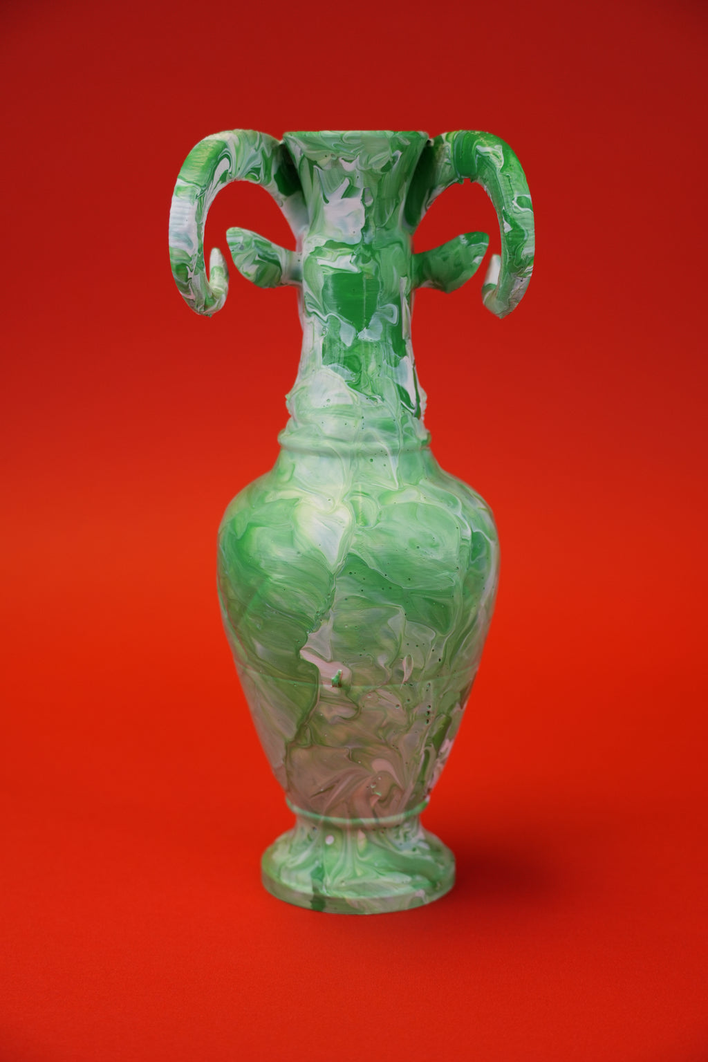 A green and white marbled ceramic vase with two curved handles, centered against a solid red background.