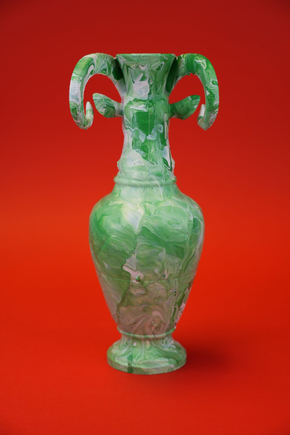 A green and white marbled ceramic vase with two curved handles, centered against a solid red background.