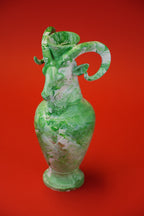A green and white marbled ceramic pitcher with a curved handle, set against a solid red background.