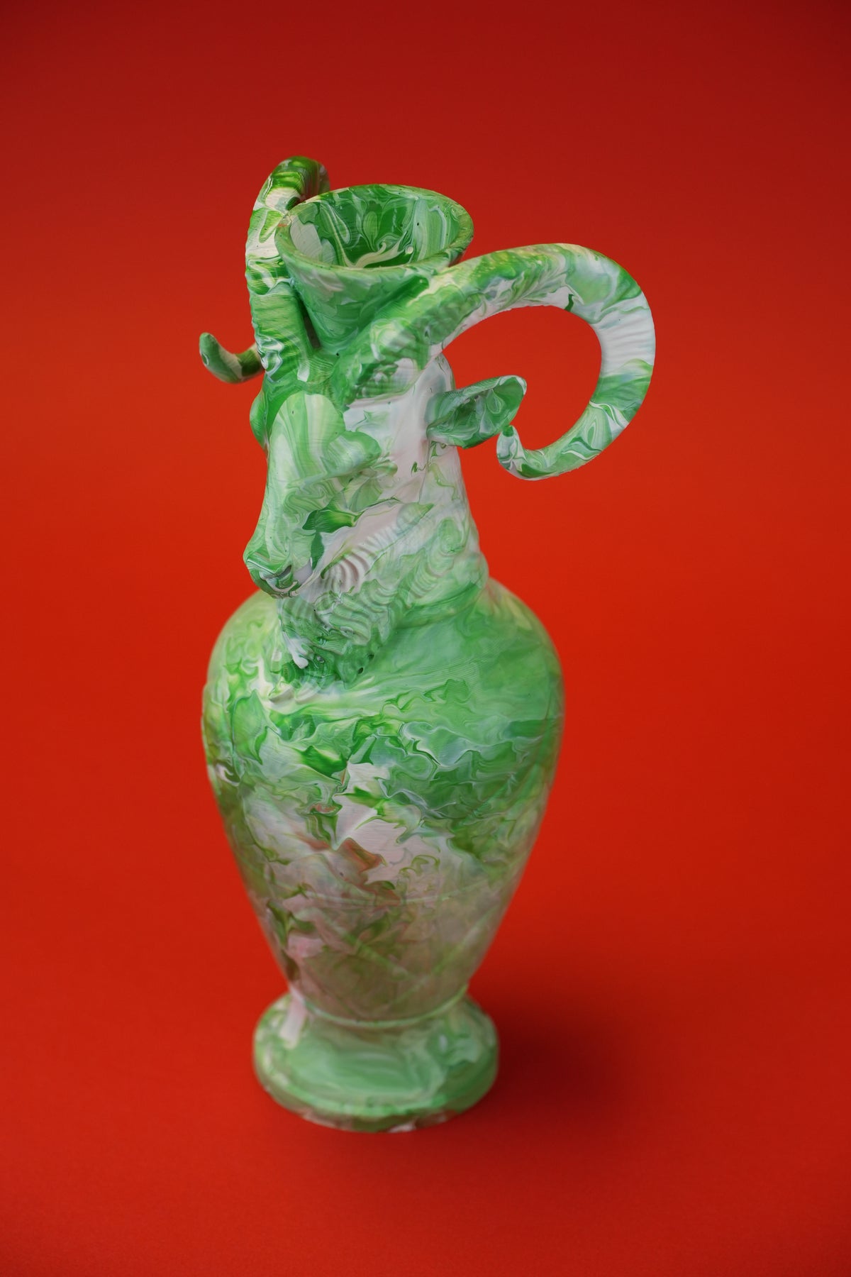 A green and white marbled ceramic pitcher with a curved handle, set against a solid red background.